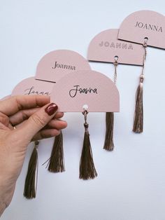 a hand holding three pink heart shaped place cards with tassels on each one