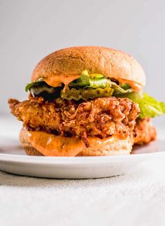 a chicken sandwich with lettuce and tomato sauce on a white plate, ready to be eaten