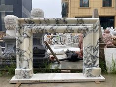 a white marble fireplace surround with sculptures in the background