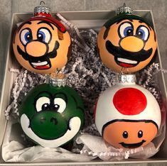 three ornaments in a box decorated with mario and luigi's face faces on them