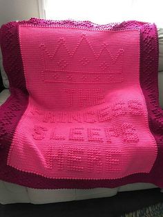 a pink crocheted blanket sitting on top of a white couch next to a window