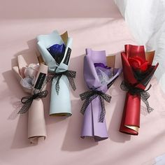 four different colored paper wrapped in ribbon on a pink surface with white sheets behind them