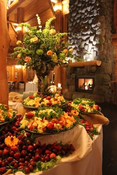 a table topped with lots of different types of fruit and vegetables next to a fire place