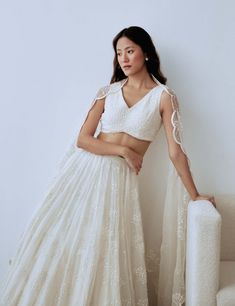 Evoke a dreamy, romantic mood with this exquisite set. It features a panelled organza skirt adorned with meticulously hand-embroidered baby’s breath motifs in ivory frosted sequins and beads. The ensemble includes a beaded v-neck sleeveless blouse, an embellished organza dupatta with an irregular cloud-like scalloped border, and delicate lace trim. This ethereal set makes a statement and adds an otherworldly touch to your look. Organza Lehenga With Lace Work For Reception, Organza Anarkali Set With Pearl Embroidery For Reception, White Tissue Silk Choli For Wedding, Off White Organza Lehenga For Reception, Pearl Embroidery Lace Sets For Wedding, Lace Sets With Pearl Embroidery For Wedding, Pearl Embroidered Lace Wedding Sets, Wedding Sets In Organza With Pearl Embroidery, Wedding Organza Sets With Pearl Embroidery