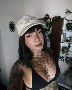 a woman with tattoos on her chest wearing a hat