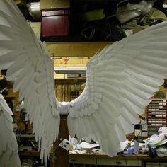 two large white angel wings sitting on top of a wooden table in a room filled with junk