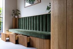 a green velvet bench sitting next to a tall wooden column in a room with large windows