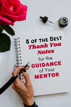 a person writing on a notepad next to a red rose and earbuds