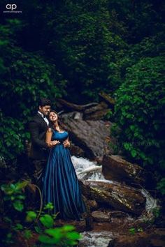 a man and woman standing next to each other in front of a river surrounded by trees