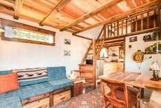 a living room filled with furniture next to a wooden table and stairs leading up to a loft