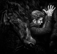 black and white photograph of a man petting a horse's head with his hands