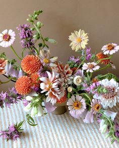 a vase filled with lots of colorful flowers on top of a striped table cloth next to a wall