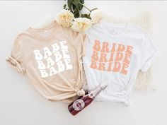 two t - shirts that say babe and bride on them next to some flowers with a bottle of booze