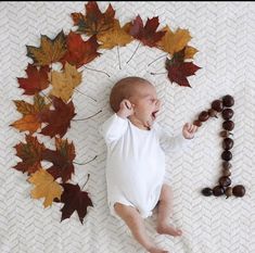 a baby laying on top of a bed next to autumn leaves and bead necklaces