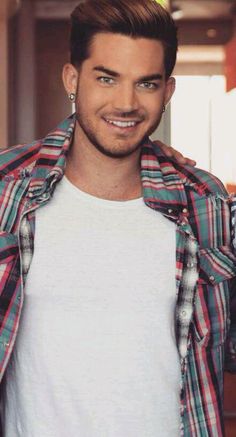 a young man is smiling while wearing a plaid shirt and ear piercings on his head