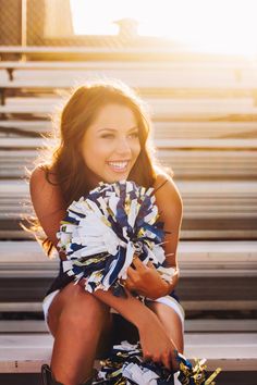 a young woman sitting on the bleachers holding a cheerleader's pom - pom