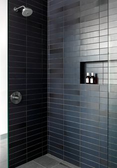 a black tiled shower with two bottles on the wall