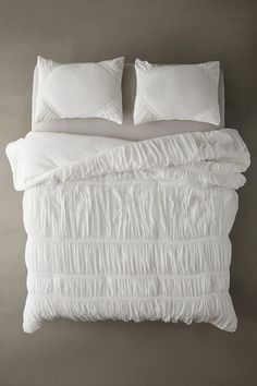 an unmade bed with two pillows and white blankets on top of it, against a gray wall