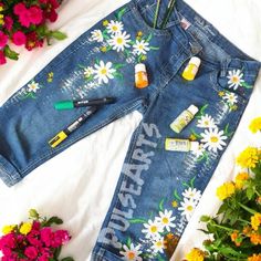 a pair of jean shorts with flowers and bottles on the side, next to some pens