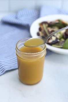 a spoon full of liquid next to a bowl of salad