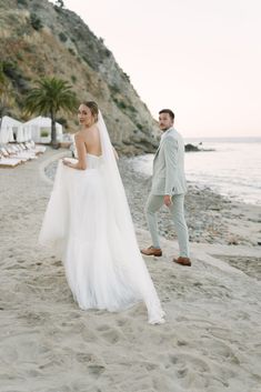 a bride and groom walking on the beach