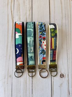 four key fobs are lined up on a white wooden surface, each with different designs and colors