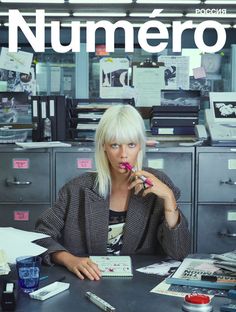 a woman sitting at a desk in front of a filing cabinet with papers on it