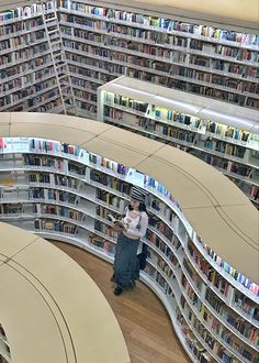 an aerial view of a woman reading in a library with bookshelves and overhead lighting