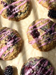 blueberry muffins with pink icing and blackberries on parchment paper next to each other