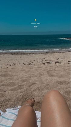 a person laying on top of a beach next to the ocean with their feet in the sand