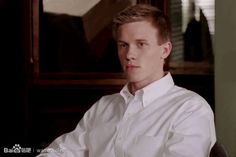 a young man sitting in front of a mirror wearing a white shirt and black pants