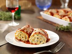 a white plate topped with lasagna rolls next to a glass of red wine