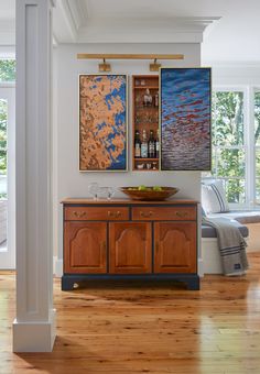 two paintings hang on the wall above a wooden cabinet in a room with hardwood floors