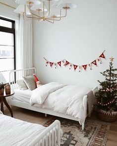 a bedroom decorated for christmas with white bedding and red garland hanging from the ceiling