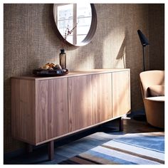 a wooden cabinet sitting in front of a round window next to a chair and lamp