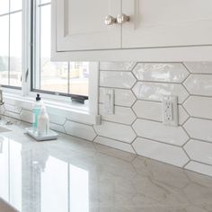 a white kitchen with marble counter tops and tile backsplashes, including a window