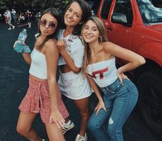 three girls standing next to each other in front of a red truck and posing for the camera