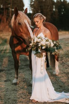 a woman standing next to a horse with flowers in her hand and holding the bridal bouquet