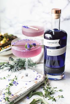 a bottle of blueberry gin next to a glass filled with the same drink and garnished with lavender sprigs