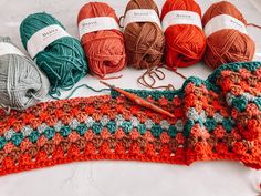 several balls of yarn and crochet needles on a white tablecloth with an orange, green, red, and blue afghan