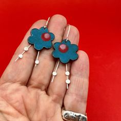 BIG BOLD peacock BLUE BLOSSOM earrings.... statement earrings for dressing up with just a bit of swing.   The silver buds swing to and fro beneath the enameled flower. Wear what you love! Handmade enamel floral earrings perfect as a birthday or anniversay gift. how they are made ... sawn, soldered, sanded,  and enameled... ..handmade and colored with ground glass these enamel earrings measure aproximately 2" long by 7/8".  * NOTE: The earring's enamel surface has tiny flecks of other colors embedded. The earrings are handmade and no two earrings are perfectly alike.  ♦ handmade ♦ ready to ship ♦ measure approximately 2" long by 7/8" wide ♦ packaged in a gift box ...the perfect gift for someone special... or yourself.  @metalobjects - brandishing a torch and hammer for fun! Blue Flower Charm Earrings, Unique Handmade Blue Flower Earrings, Bohemian Blue Enamel Earrings, Blue Enamel Flower Earrings As Gift, Unique Blue Flower Earrings With Ear Wire, Unique Blue Earrings, Blue Flower-shaped Hand Painted Earrings, Blue Hand Painted Flower Earrings, Turquoise Flower Earrings