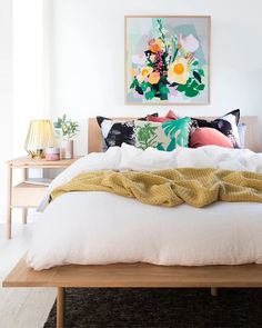 a bed with white sheets and pillows in a bedroom next to a painting on the wall