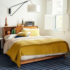 a bed with yellow blankets and pillows in a bedroom next to a window that reads west elm