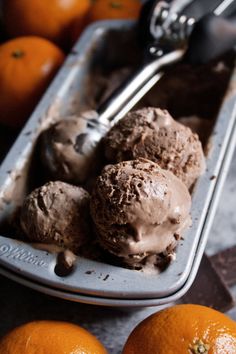 three scoops of ice cream in a tray with oranges and spoon on the side