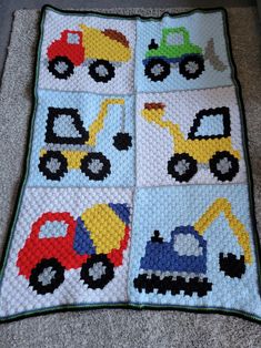 a crocheted baby blanket with trucks and cars on it, sitting on the floor