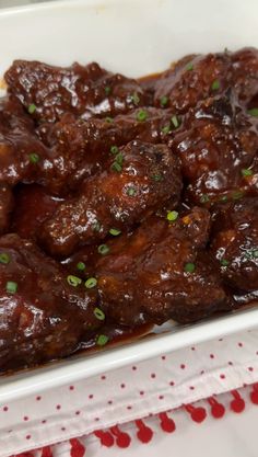 a white plate topped with meat covered in sauce and garnished with scallions