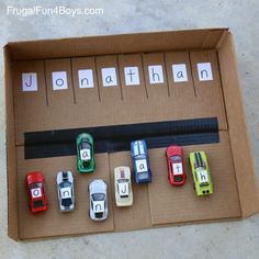 a cardboard box filled with toy cars sitting on top of a cement floor next to letters that spell out the word jonathan