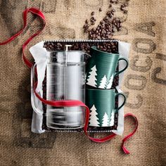 two coffee mugs in a gift box with red ribbon on the bottom and white trees printed on them