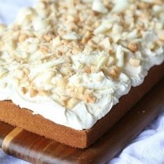 there is a cake with white frosting and nuts on the top, sitting on a cutting board