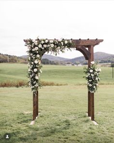 a wooden arch with flowers and greenery on it in the middle of a field